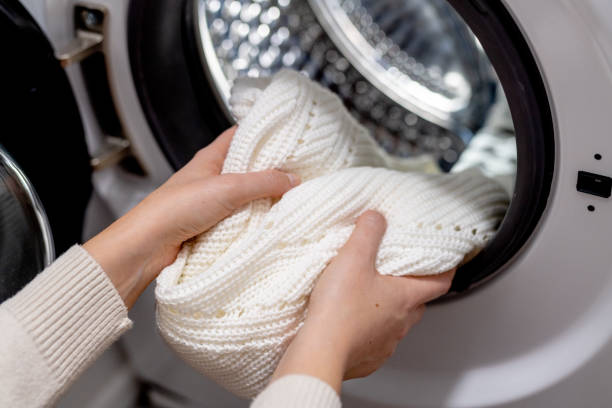 Woman putting white clothes into the drum of a washing machine, front view. Washing dirty clothes in the washer